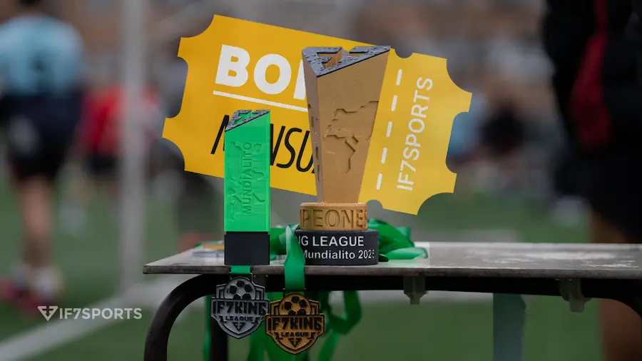 Trofeo del Mundialito IF7SPORTS junto a medallas y bono mensual sobre una mesa en el campo de fútbol