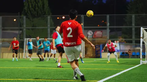 Player kicking a ball in an amateur football match on a floodlit field